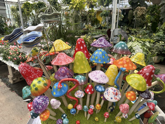 Colorful display of handmade ceramic Shroomyz mushroom and Wormyz garden stakes by JJ Potts Studio at a greenhouse
