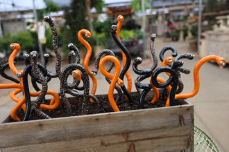 Yellow, blue, and red JJ Potts Studio ceramic Wormyz garden stakes winding through variegated hosta leaves