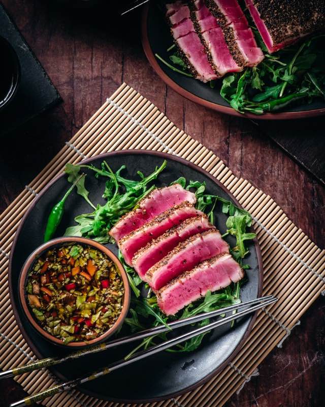 Seared ahi tuna plated on a Jefferson Street black ceramic plate with arugula and pickled vegetables