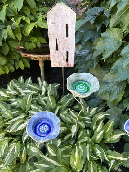 Green and blue ceramic Flower Puddler garden stakes by JJ Potts Studio planted in a variegated hosta bed