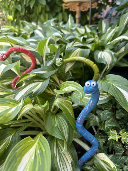 Close-up of red, blue, and green ceramic Wormyz garden stakes from JJ Potts Studio among garden foliage