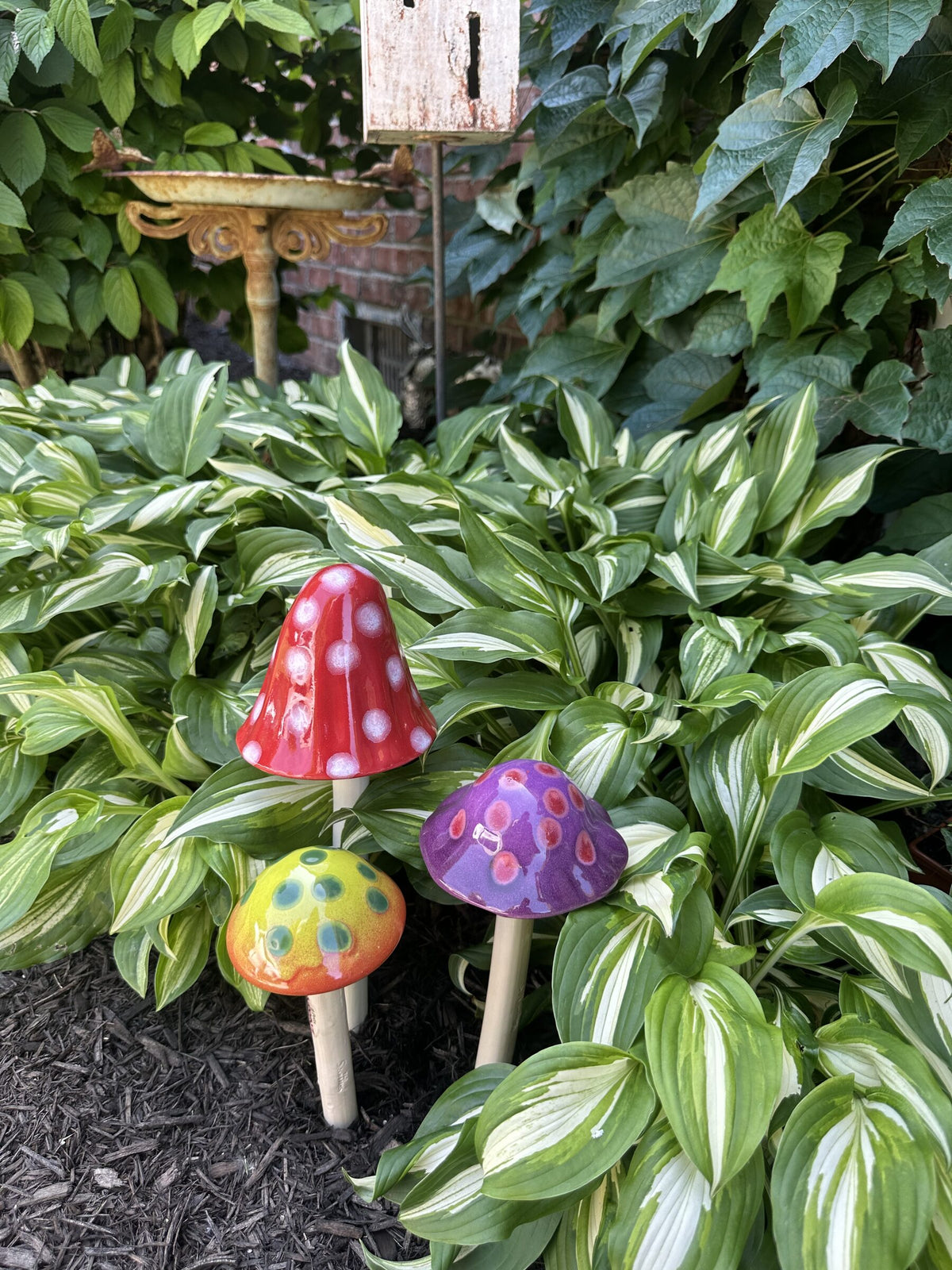 Purple, red polka-dot, and lime ceramic Shroomyz mushroom garden stakes by JJ Potts Studio in a shaded hosta bed