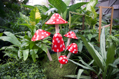 Red polka dot Shroomyz ceramic mushroom garden stakes grouped in a lush greenhouse planting