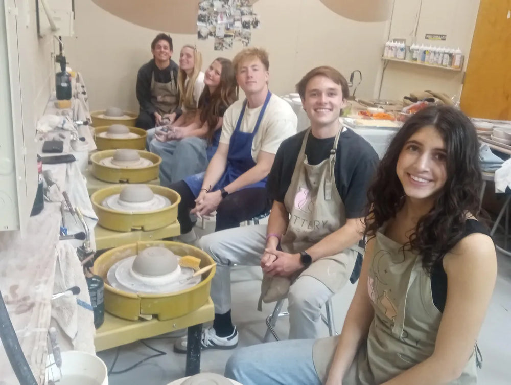 Five students smiling at pottery wheels