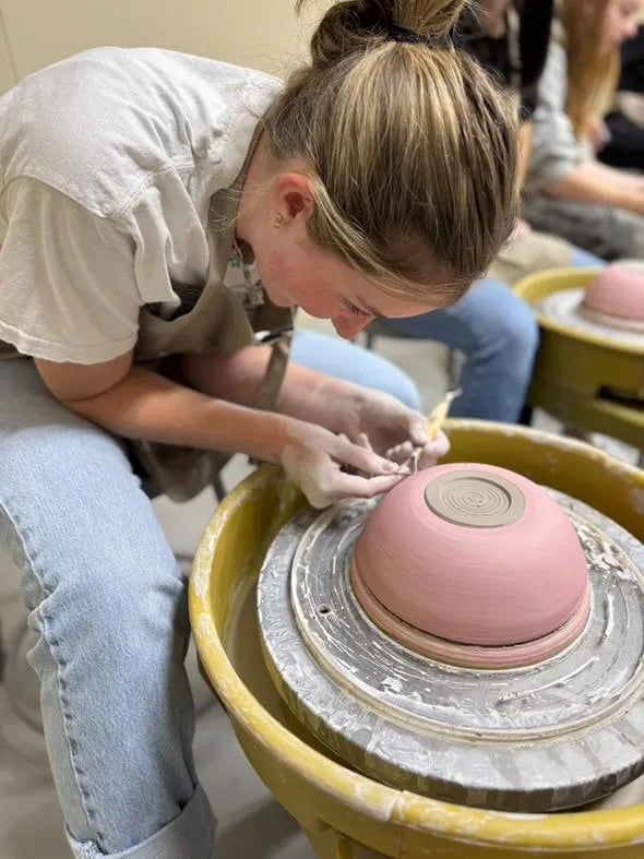 Student shaping a pink bowl on the wheel