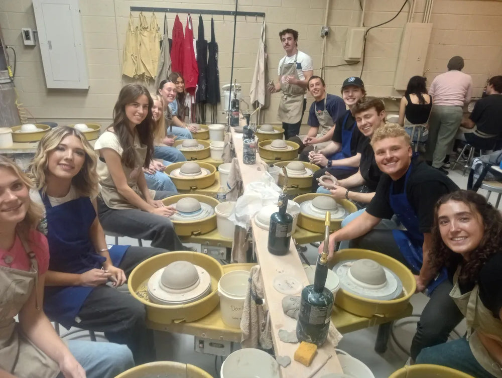 Class of pottery students smiling at the wheels