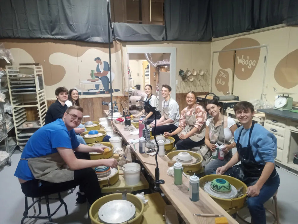 Group of pottery students smiling at wheels with Wedge sign